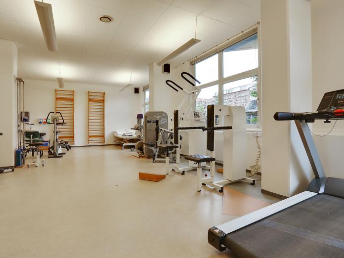 Lyst motionsrum med forskellige træningsmaskiner som løbebånd og kondicykel samt ribber på endevæggen.