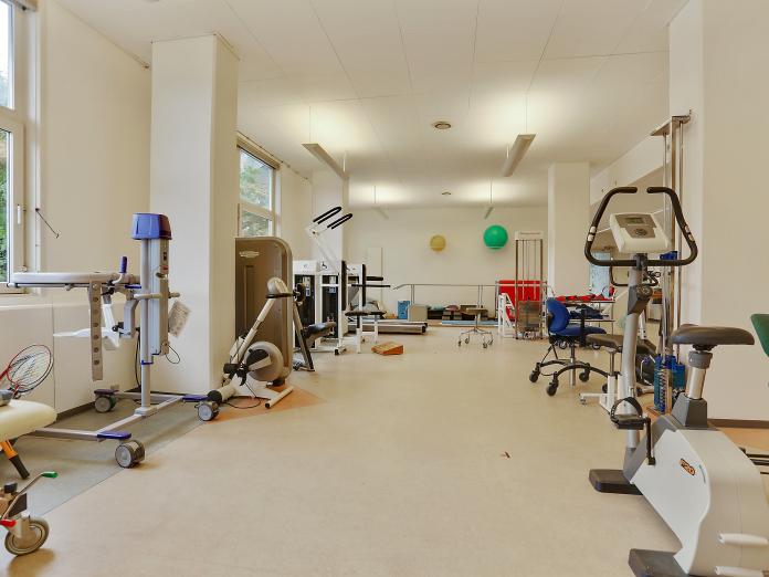 Lyst motionsrum med forskellige træningsmaskiner som kondicykler samt gangbarre, briks og pilatesbolde.