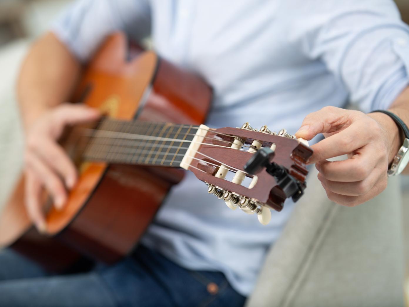 Mand iklædt blå skjorte og cowboybukser sidder med guitar på skødet.
