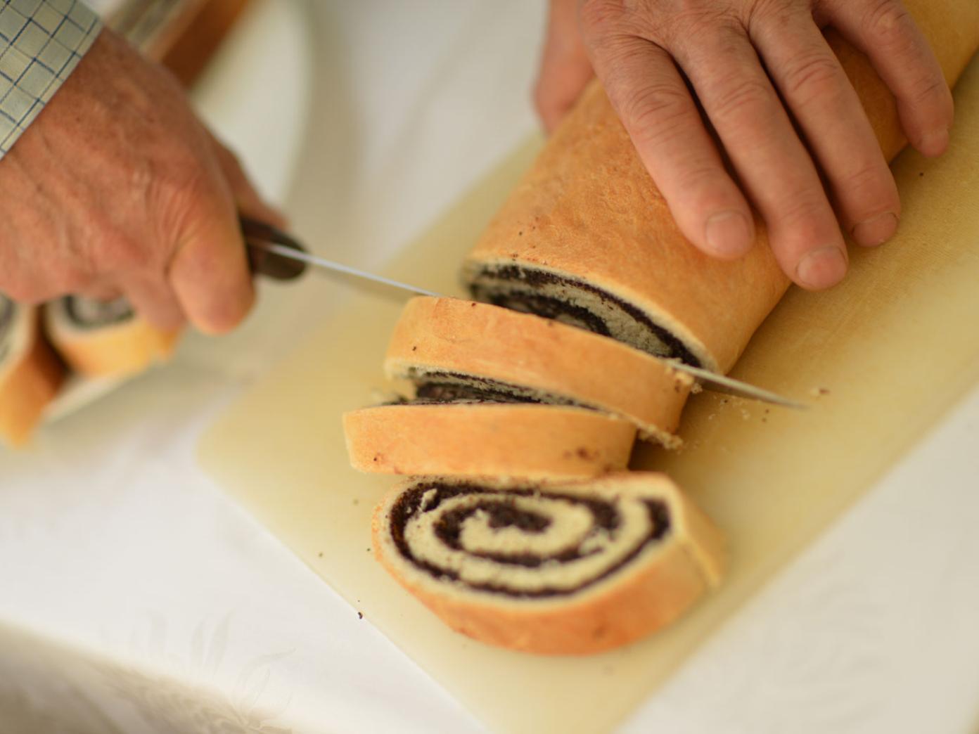 Hjemmebagt chokoladeroulade bliver skåret i skiver af ældre person.