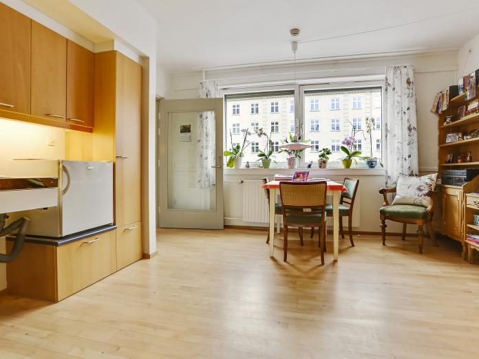 Tekøkken, lille spisebord, vinduer, en lænestol og en reol.