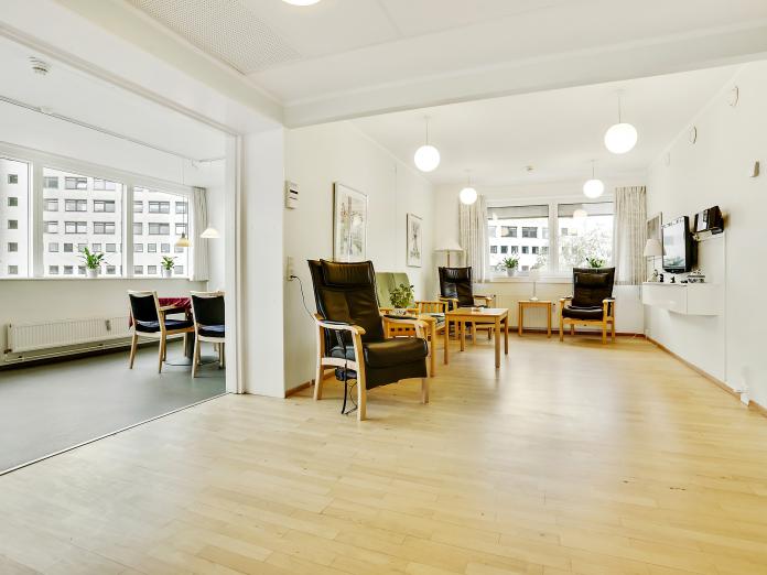 Fællesrum med lænestole, små borde og tv. 