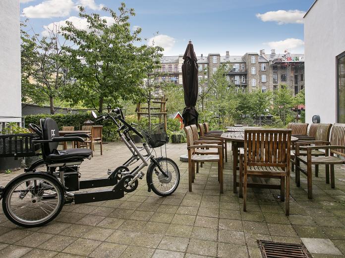 Duocykel og terrasse med havemøbler i træ og kig til gården.