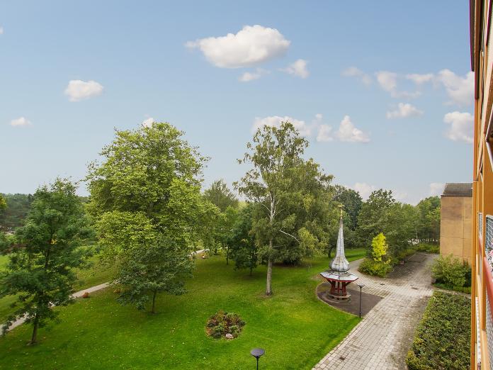 Grøn park med græsplæner, høje træer, buske, hække og gangstier.