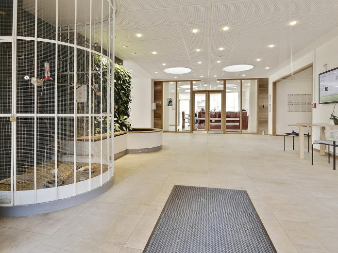 Lyst, rummeligt indgangsområde med voliere, grøn plantevæg og siddepladser.