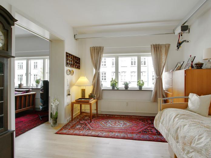 Lyst soveværelse med plejeseng, loftslift og personlige møbler som chatol og bornholmerur.