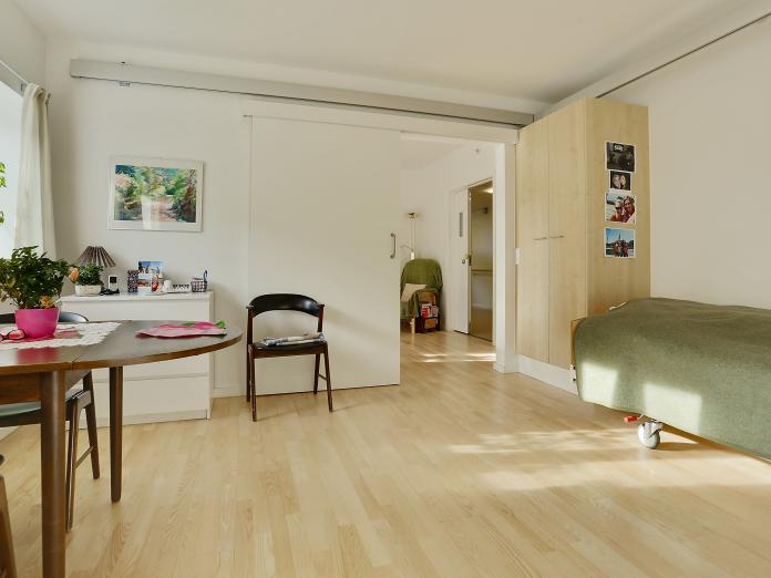 Lyst værelse med plejeseng, loftslift og indbyggede skabe. Værelset er desuden indrettet med personlige møbler som spisebord med stole og kommode.