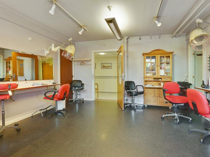 Frisørsalon med tre klippestationer, tørrehjelme og spejle.