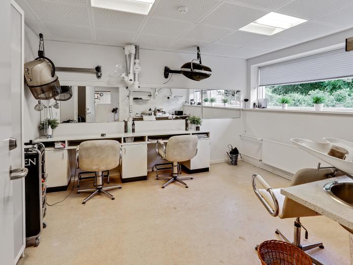 Frisørsalon med to stole, en vask med stol og forskellige remedier, der hænger i loftet.