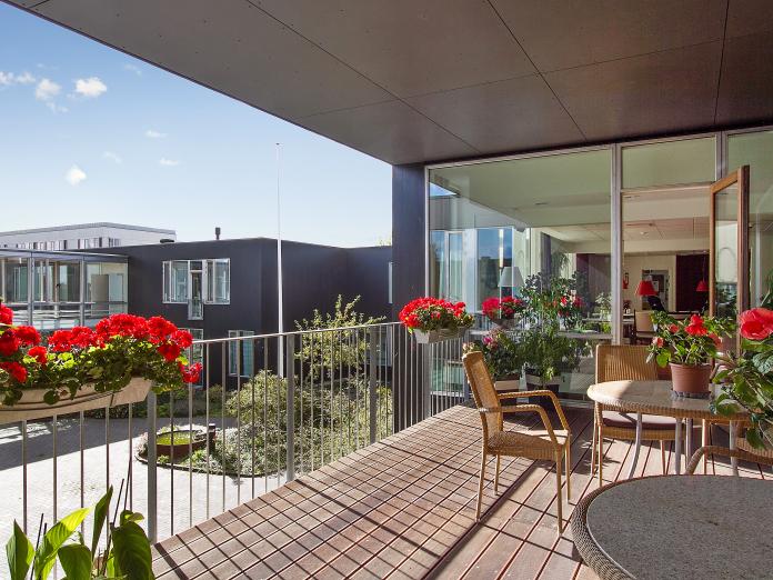 Fælles altan med røde blomster i altankasser, havestole og havemøbler.