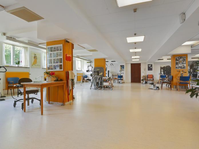 Stort motions- og aktivitetsrum med forskellige motionsmaskiner, gangbarre og grønne planter.