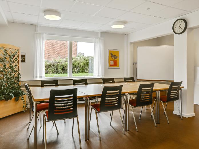 Lyst rum med aflangt bord med stole omkring og et whiteboard.