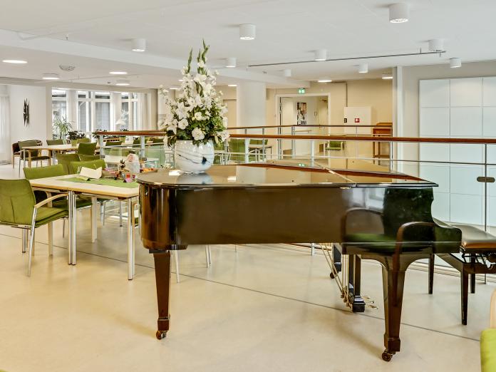 Stort, lyst fællesområde med flere siddepladser omkring mindre borde samt et flygel.