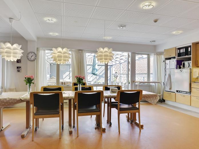 Fælles køkkenområde med langt spisebord og dør åben ud til altan.