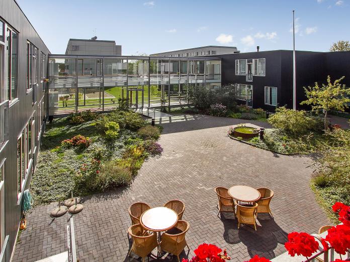 Kig ned på en stor terrasse med havemøbler og store bed med forskellige planter, blomster og træer.