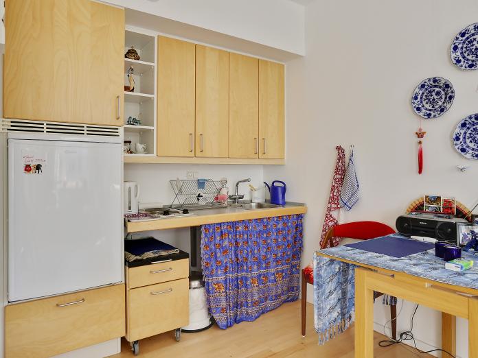 Tekøkken med vask og to kogeplader i bordpladen samt køleskab, overskabe og skuffemodul på hjul.