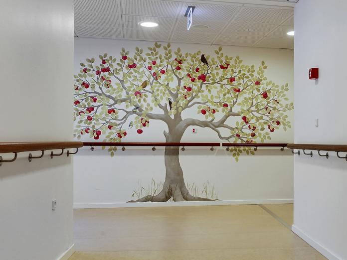 Gangareal med gelænder i mørkt træ og på væggen er malet et stort træ med røde æbler og en solsort.