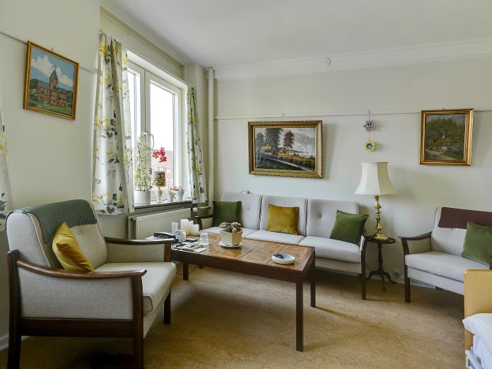 Lys stue møbleret med sofa, lænestole og sofabord samt malerier på væggene.