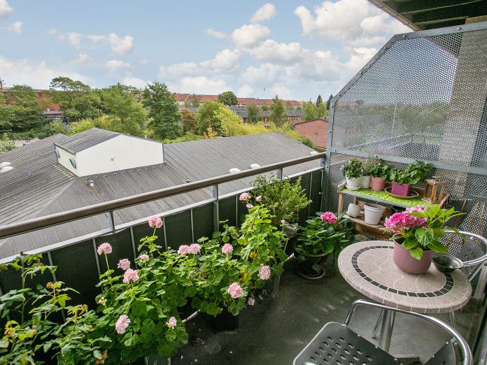 Privat altan med mange blomster i krukker samt cafébord og stole.