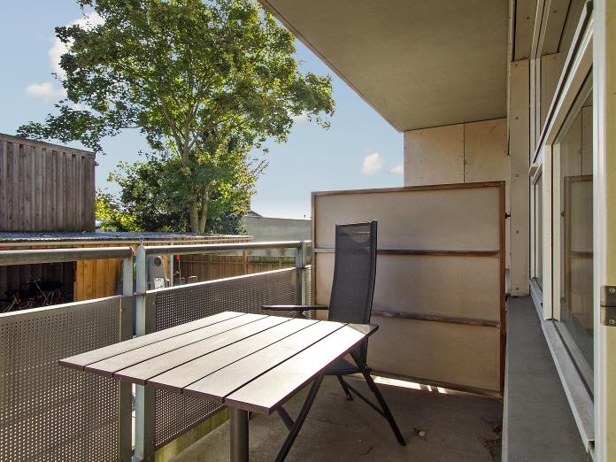 Overdækket altan med altanmøbler. Fra altanen er der kig ned i en gård og over på et stort træ.