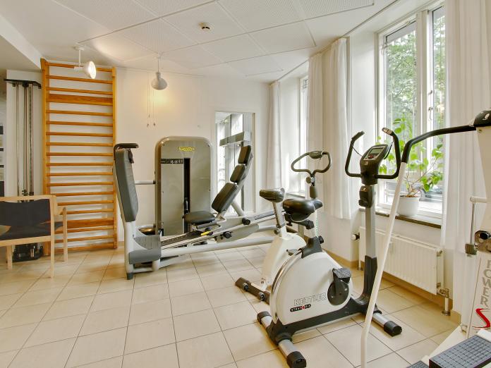 Lyst motionsrum med forskellige træningsmaskiner som kondicykler samt en ribbe og et spejl.