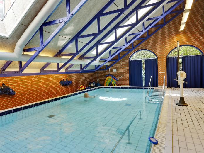 Svømmehal med et svømmebassin, der indeholder en gangbarre, samt en lift på kanten af bassinet.