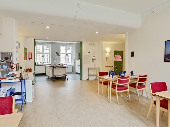 Fælles spiseområde med firmandsborde og stole og åbning ud til stort køkken.