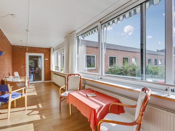 Gangareal med store vinduespartier med markiser samt hyggekroge med stole, kurvesofa og borde. 