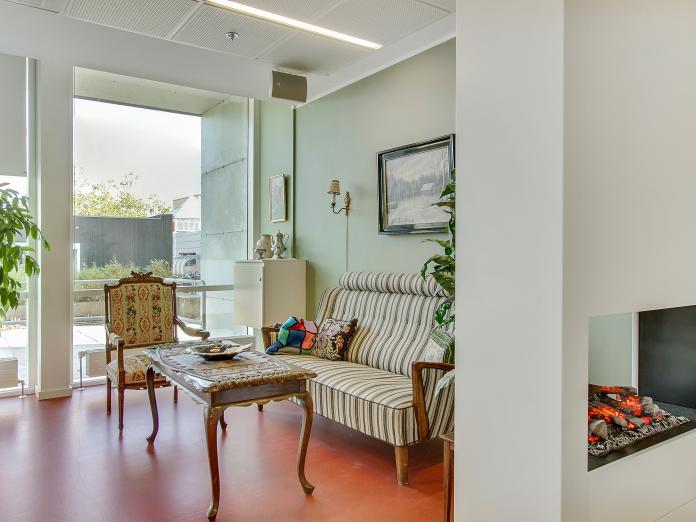 Lille, fælles hyggekrog med en sofa, lænestol, sofabord og en lille, kunstig pejs.