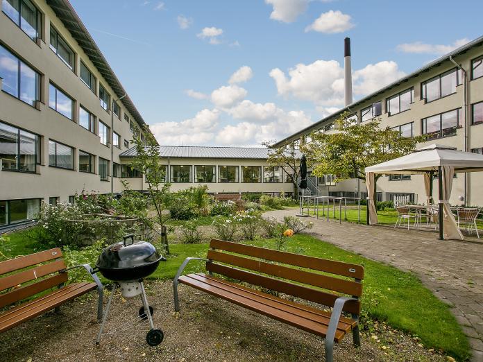 To bænke, en kuglegrill, pavillon og Bispebjerghjemmets bygninger.