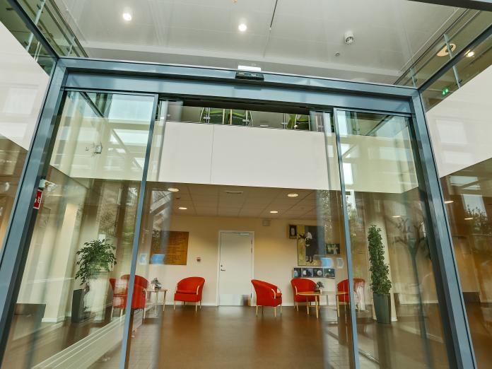 Indgangsparti i glas og hyggekroge med lænestole og borde samt store krukker med grønne planter.