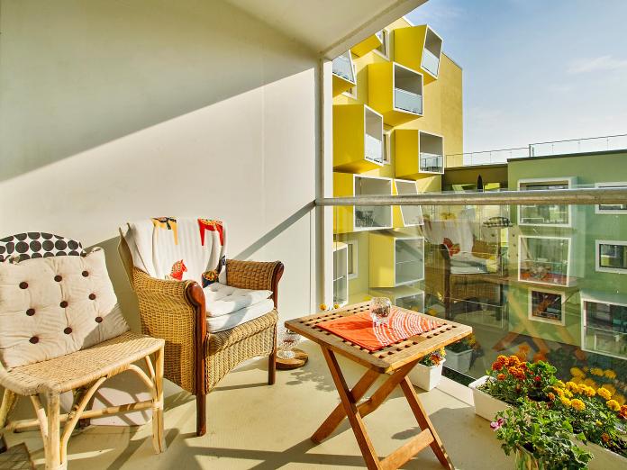 Overdækket altan med glasfacade. Altanen er indrettet med kurvestole og klapbord samt altankasser og krukker med blomster.