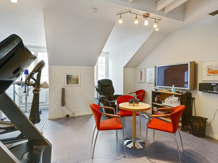 Motions- og afslapningsrum indrettet med træningsmaskiner og massagestol samt et væghængt fjernsyn og cafébord med stole omkring.