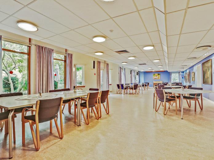 Stort fællesområde med borde og stole. Nogle af væggene er malet blå, og der hænger mange malerier på væggene. 