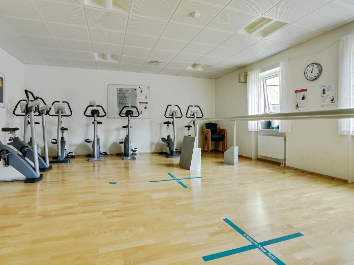 Lyst motionsrum med motionscykler og gangbarre.