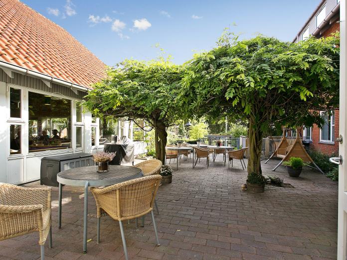 Terrasse med hængesofa, kurvestole og runde borde samt træer og blomster i krukker.