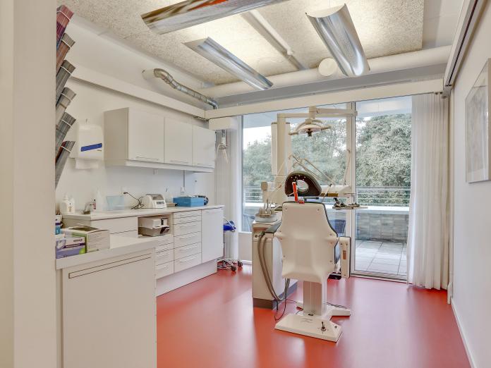 Rum indrettet som tandlægeklinik med tandlægestol, sug og bor samt skabe og skuffer til redskaber og instrumenter. Rummet er lyst med orange gulve, og fra stolen er der udsigt til træer gennem gulv til loft-vinduer.
