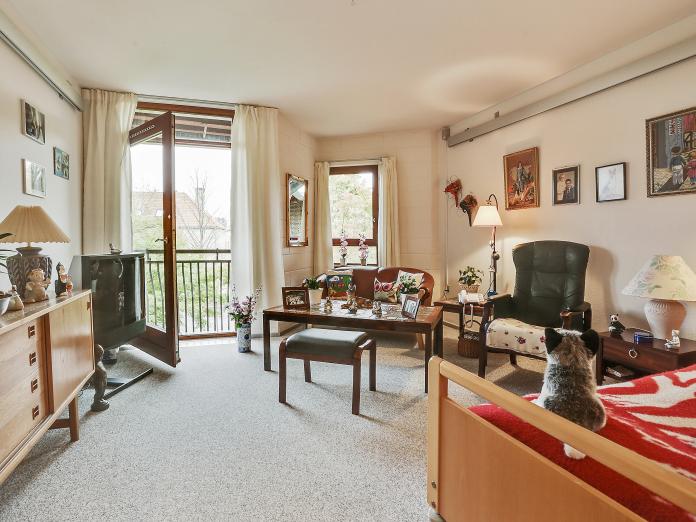 Lyst værelse med gulvtæppe og store fransk altan med bør, der åbner ind i rummet samt personlige møbler og billeder på væggen. 