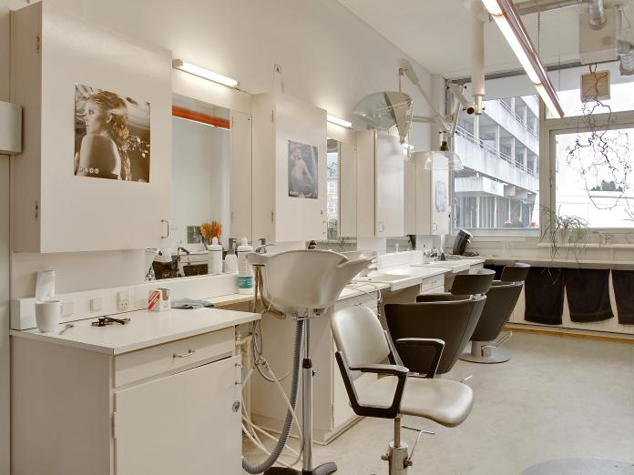Frisørsalon med stort vinduesparti samt vaskestol og to klippestationer med spejl og udsugning. 