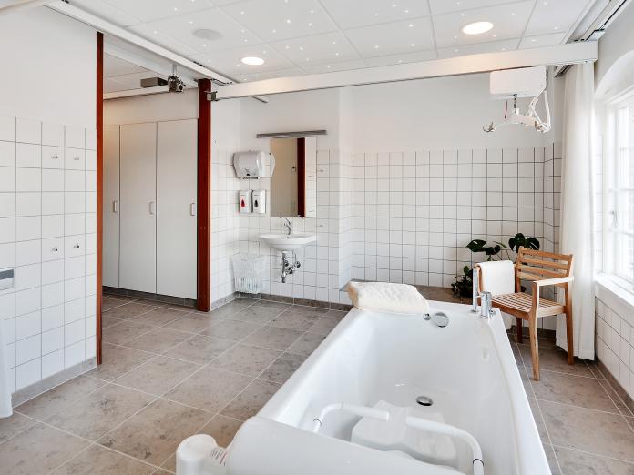 Wellness-rum med fliser på gulv og vægge samt loftslift, karbad, grønne planter og indbyggede skabe.