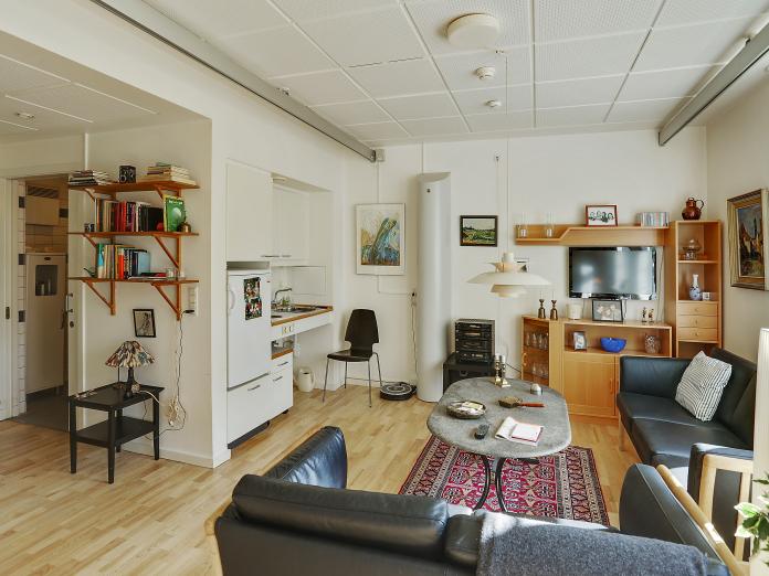 Stort, lyst værelse med tekøkken og personlige møbler som sofaer, sofabord og reolsystem.