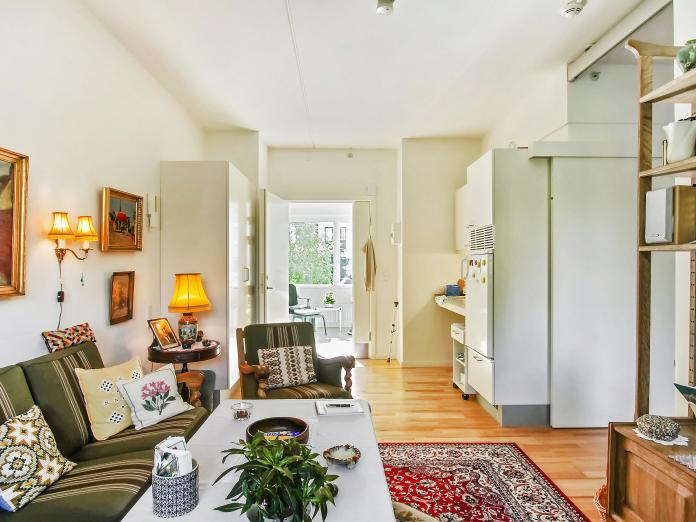 Lys stue med tekøkken og indbyggede skabe. Stuen er indrettet med personlige møbler som sofa, sofabord og lænestol.