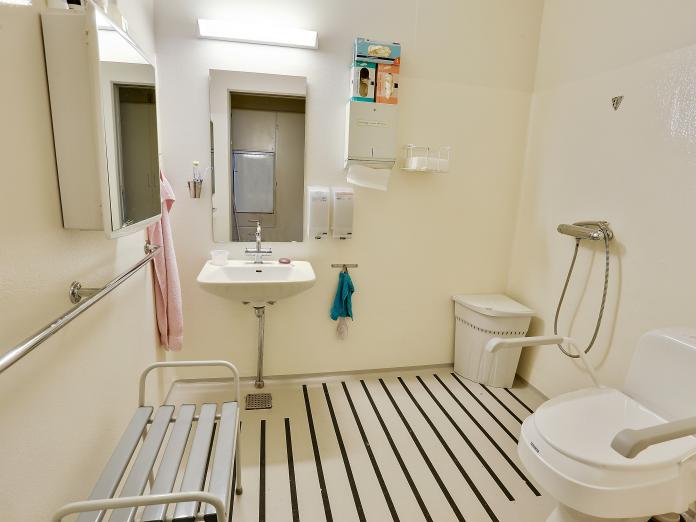 Hvidt badeværelse med spejl, vask, toilet og bruser. 