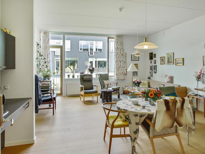 Stue med tekøkken, spisebord, sofa, lænestole og vinduer.