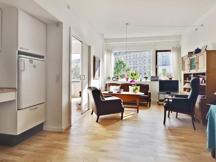 Lys stue med tekøkken med køleskab og vask. Stuen er indrettet med personlige møbler som sofa, lænestole og sofabord. Fra stuen er der adgang til soveværelset.