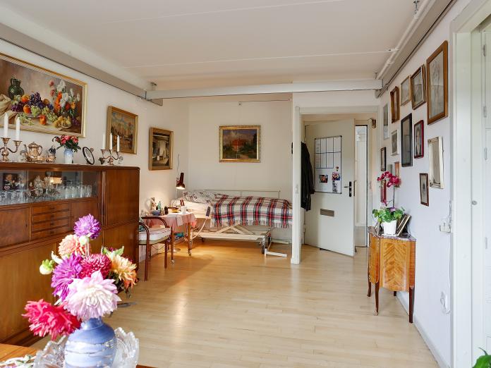 Værelse med hvide vægge og lyse parketgulve samt seng og loftslift. Værelse er møbleret med personlige møbler og malerier på væggene.