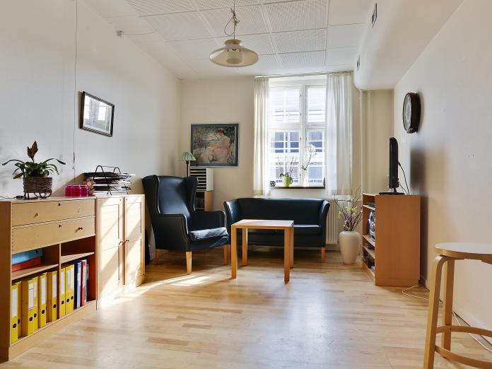 Lys stue med sprosset vindue indrettet med personlige møbler som sofa, lænestol og sofabord samt fjernsyn og reolsystem.