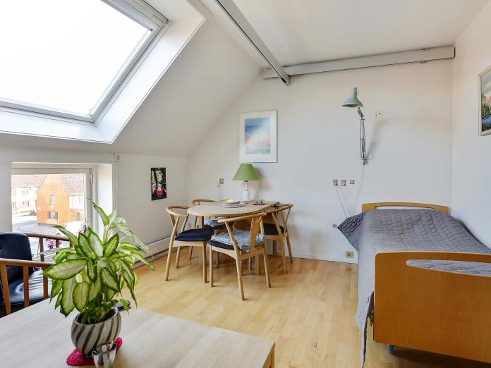 Lyst værelse med ovenlysvindue, loftslift og plejeseng samt personlige møbler som bord og stole, sofabord og lænestol.