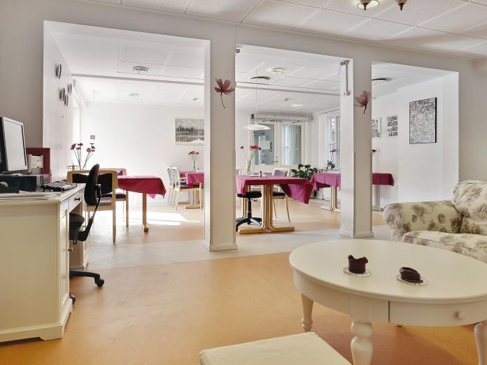 Fællesområde med computer, sofa og caféborde med dug og stole omkring. 