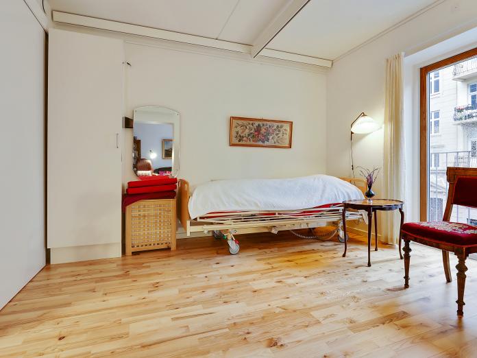 Soveværelse med hvide vægge og lofter samt lyst parketgulv og fransk altan. Værelset har desuden en loftslift, seng og indbygget skab.